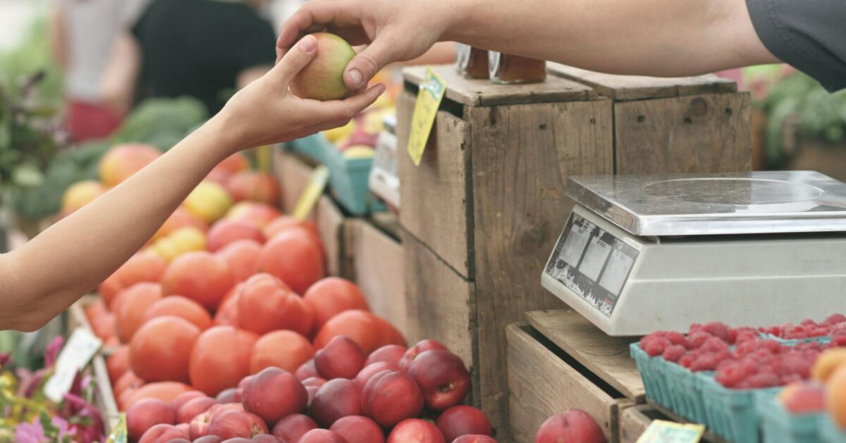 A customer exchanges an apple with a vendor at a vibrant farmers market.
